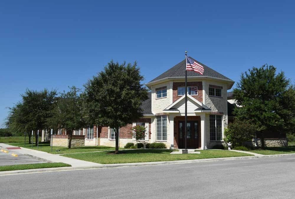 Building with brick and stone exterior, American flag, trees, sidewalk, and blue sky.