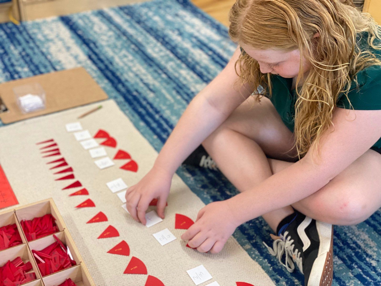 A young girl is sitting on the floor wotking montessori red triangles.
