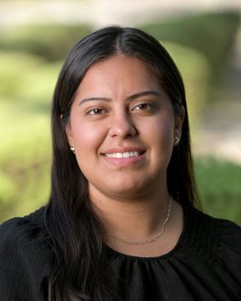 A woman wearing glasses and a cross necklace is smiling for the camera.