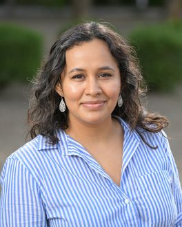 A woman wearing a blue striped shirt and earrings is smiling for the camera.