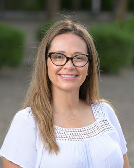 A woman wearing glasses and a white shirt is smiling for the camera.