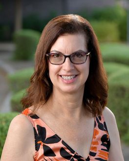 A woman wearing glasses and a floral dress is smiling for the camera.