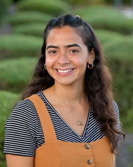 A woman in a striped shirt and overalls is smiling for the camera.