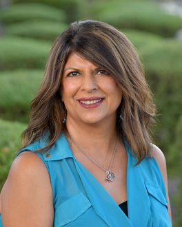 A woman in a blue shirt and necklace is smiling for the camera.