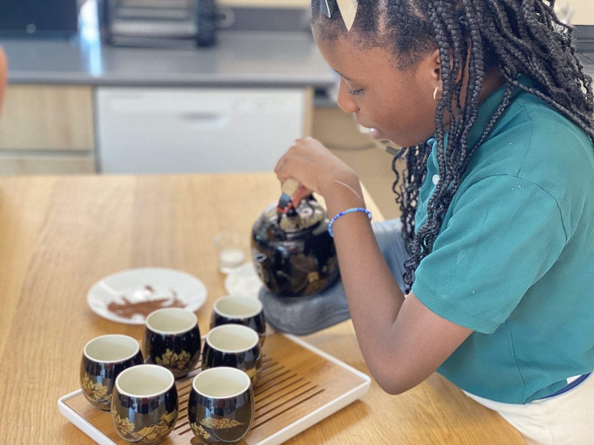 A young girl is sitting at a table pouring tea into cups.
