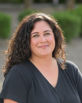 A woman with curly hair is wearing a black shirt and smiling.