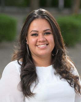 A woman wearing a white shirt and hoop earrings is smiling for the camera.