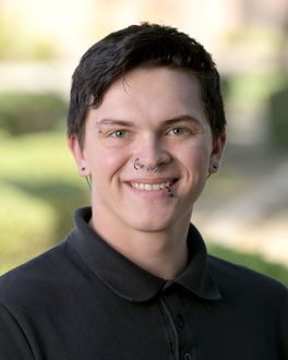 A young man wearing glasses and a black polo shirt is smiling for the camera.