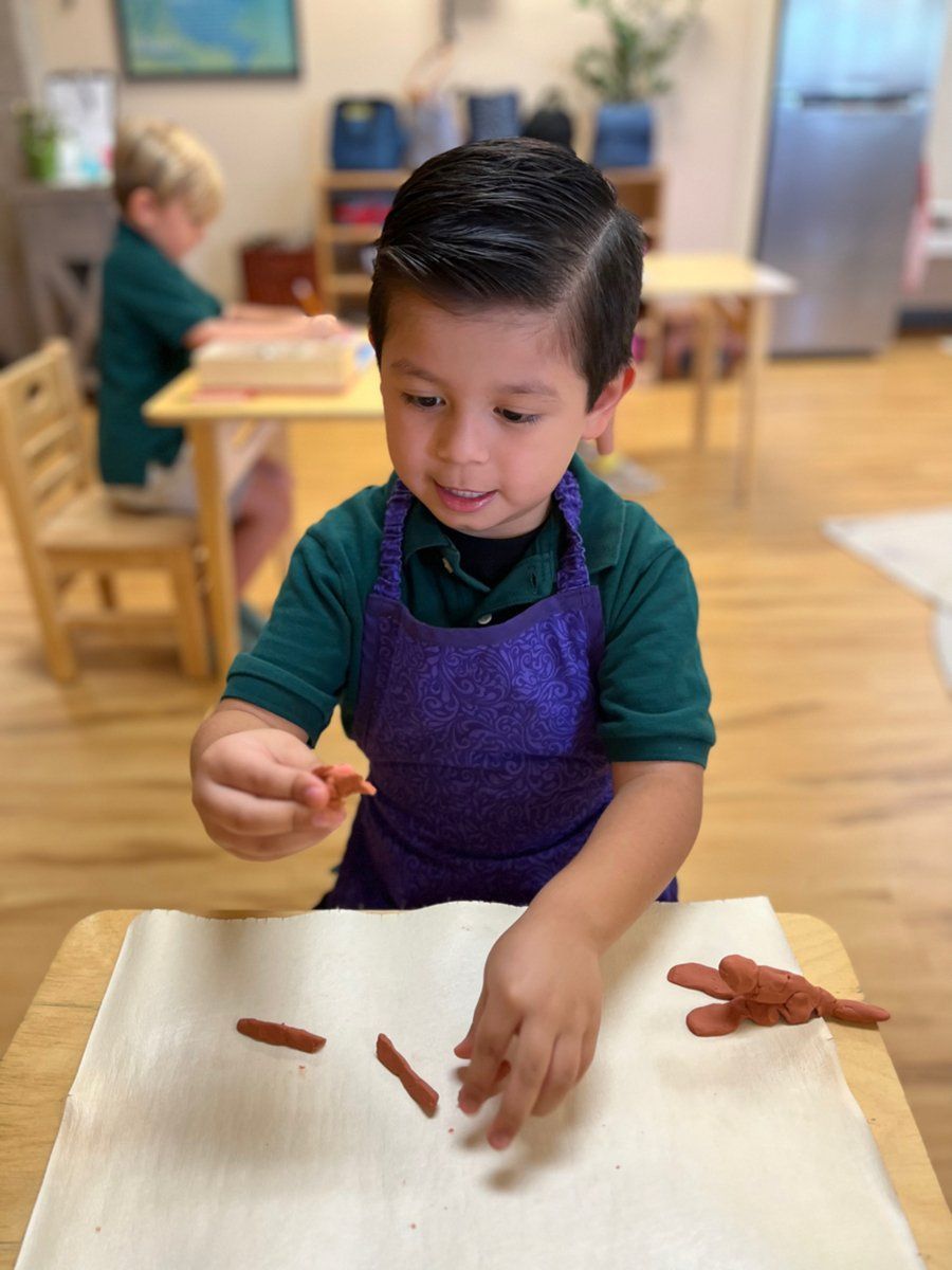 A young boy is sitting at a table playing with clay