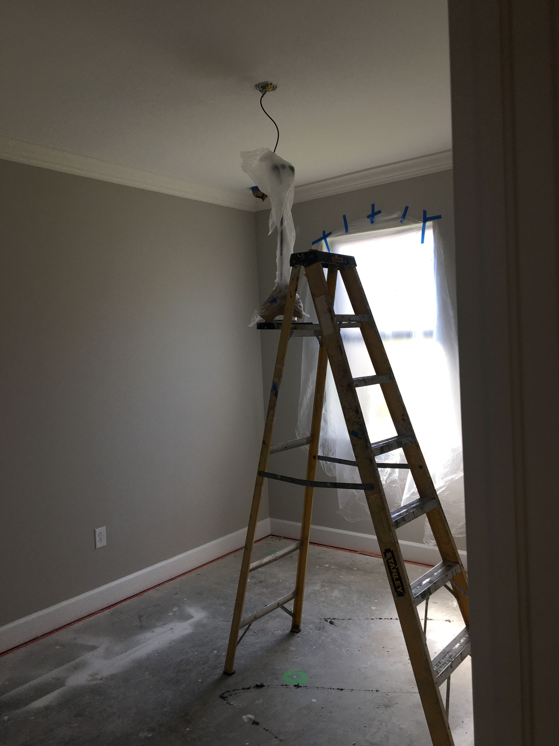 Room prepared for exterior painting services near you, with a ladder and taped window for ceiling work.