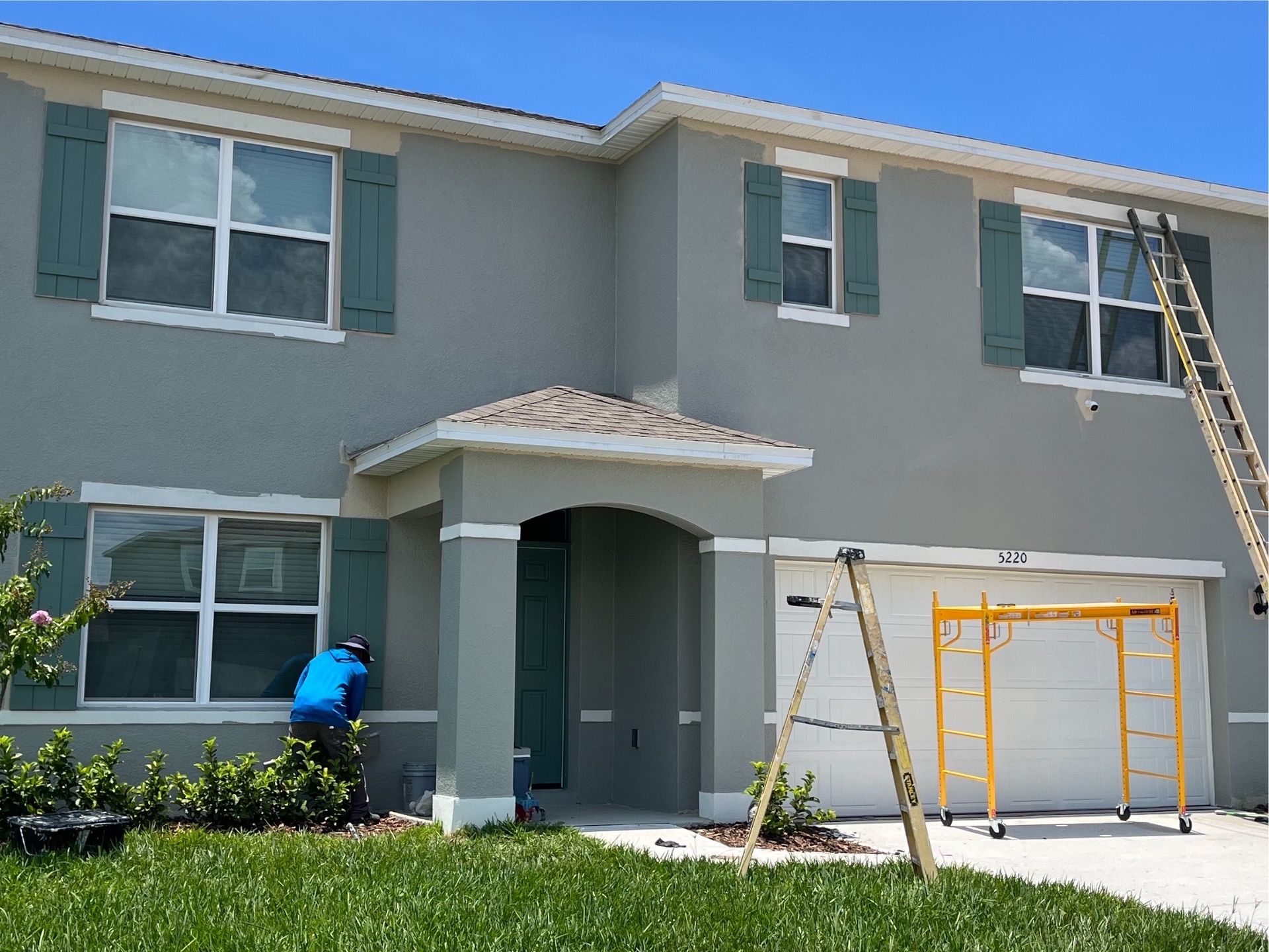 Professional exterior painting services near you, with a contractor painting a two-story home using scaffolding and ladders.