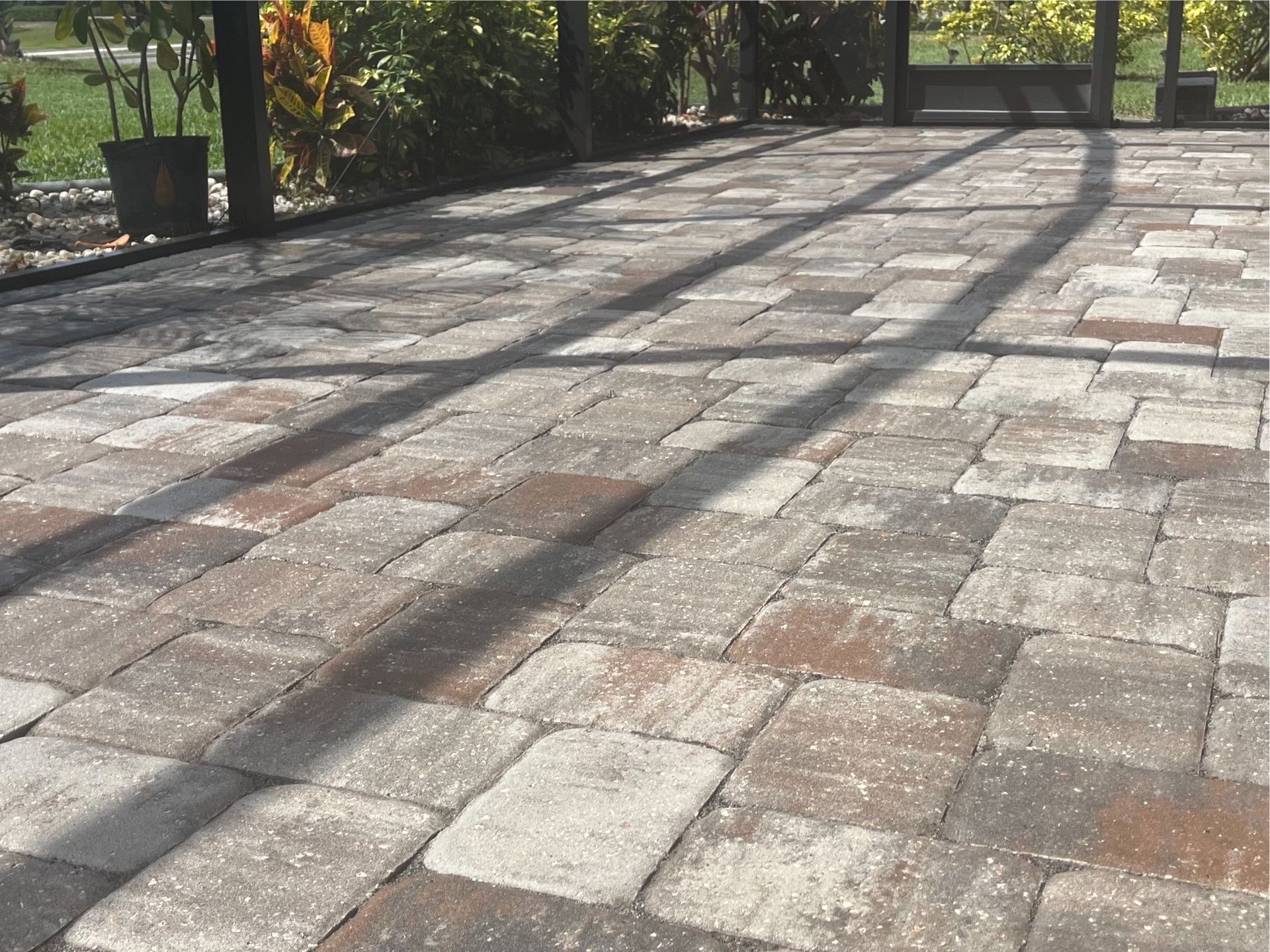 A brick patio with a screened in area and trees in the background.