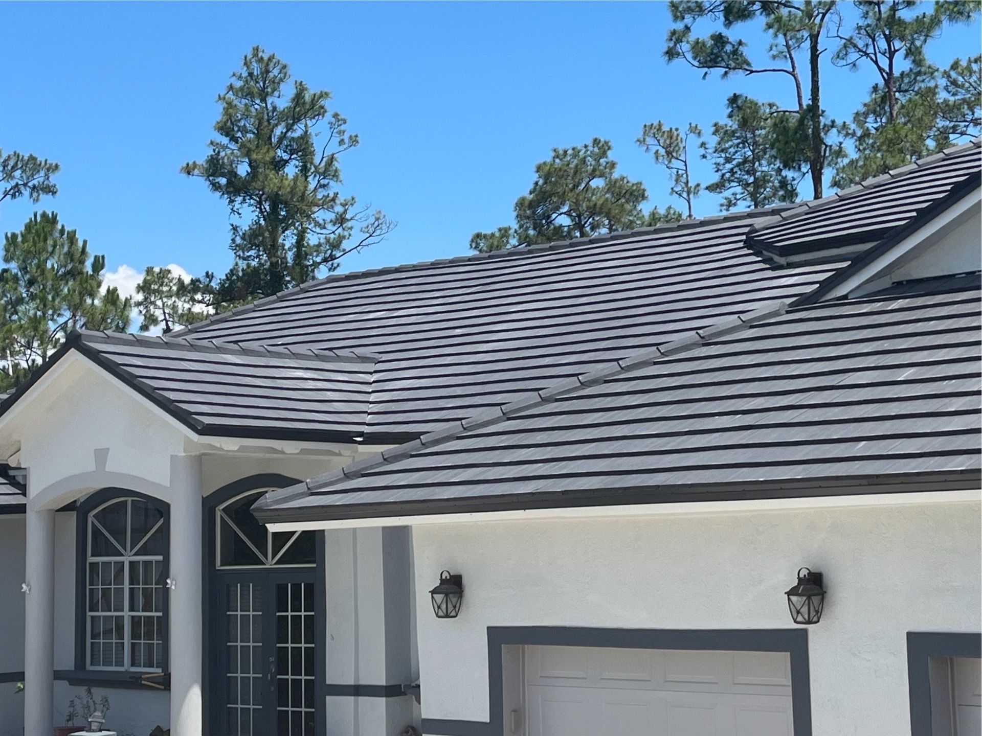 A white house with a gray roof and trees in the background
