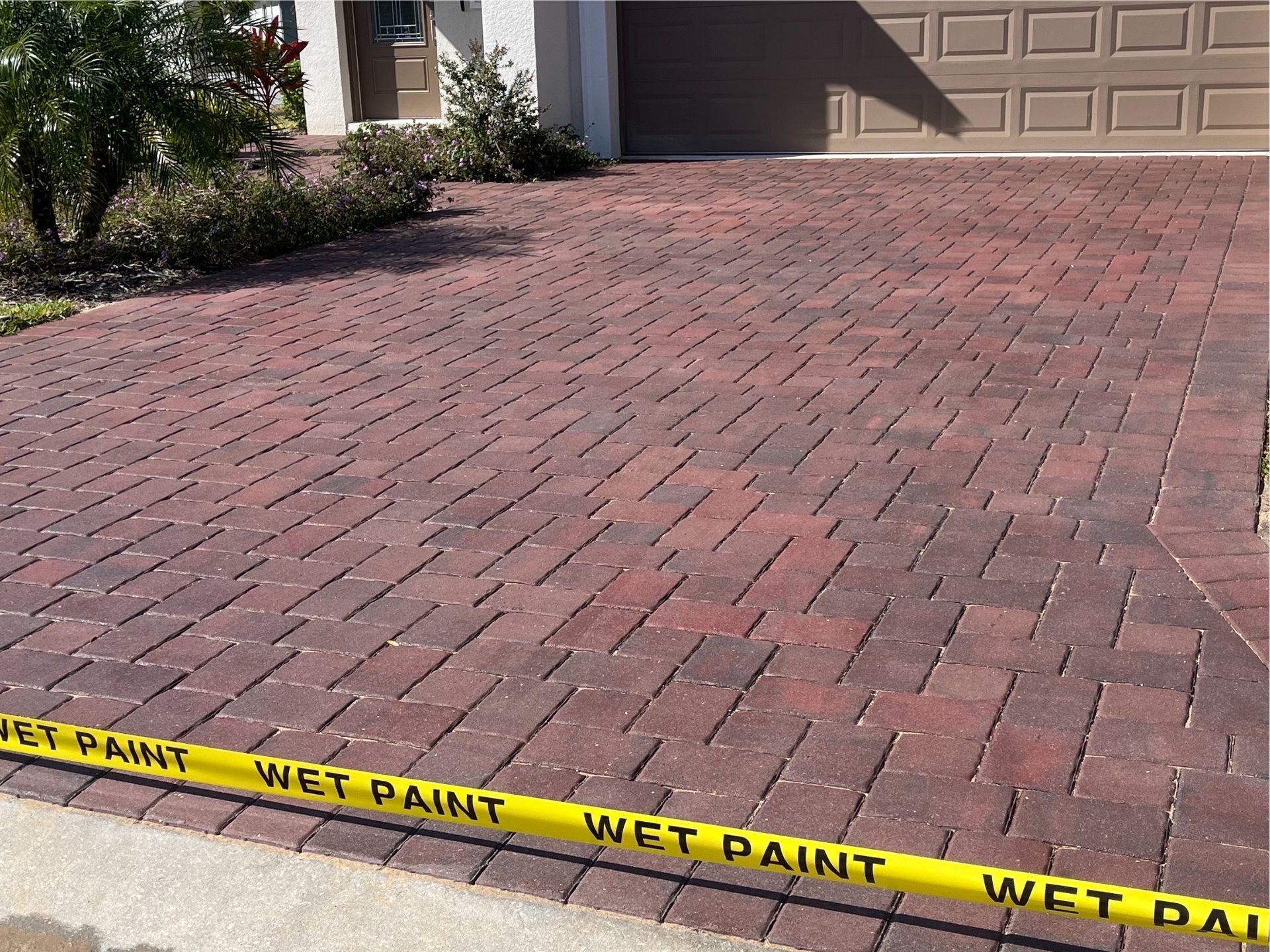 A brick driveway with a yellow tape that says wet paint