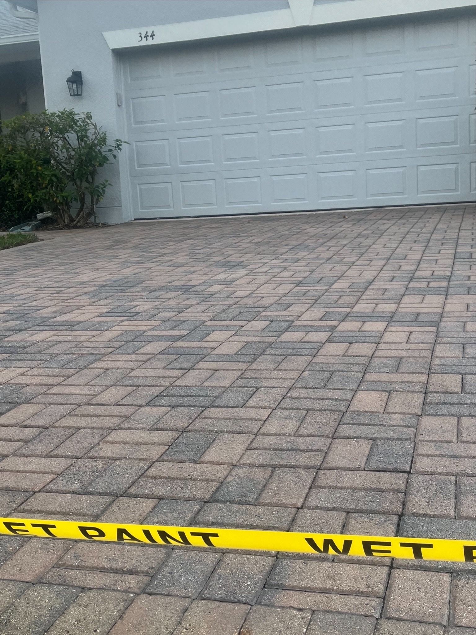 A yellow tape is laying on a brick driveway in front of a garage door.
