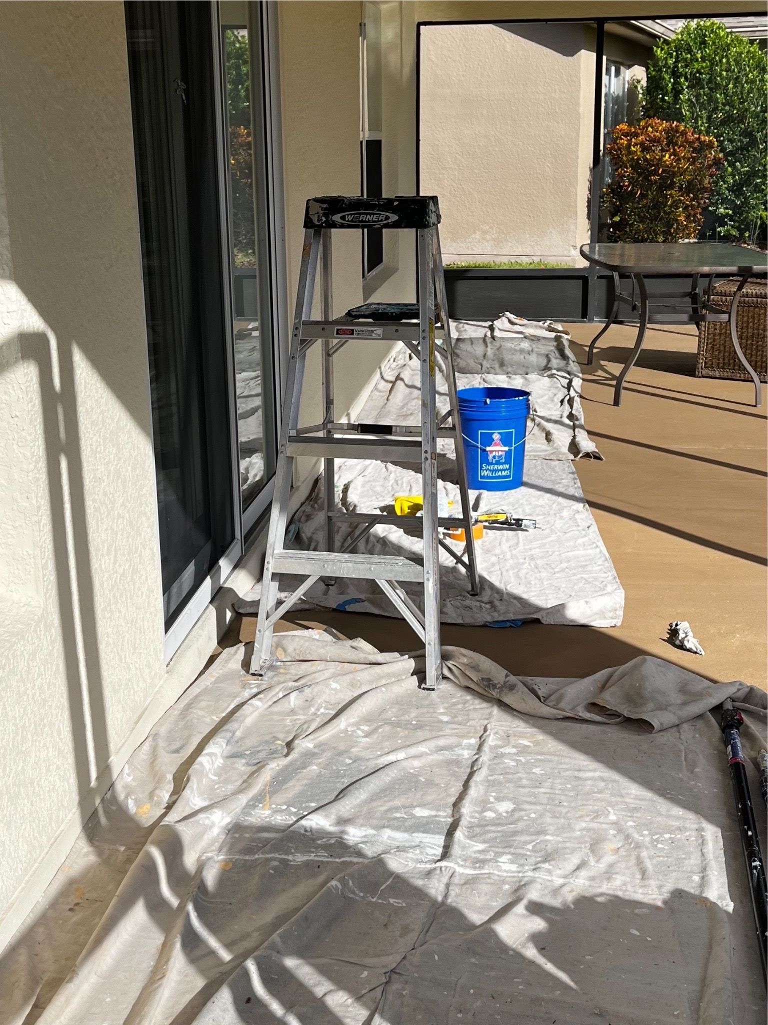 A ladder is sitting on a covered patio next to a blue bucket.