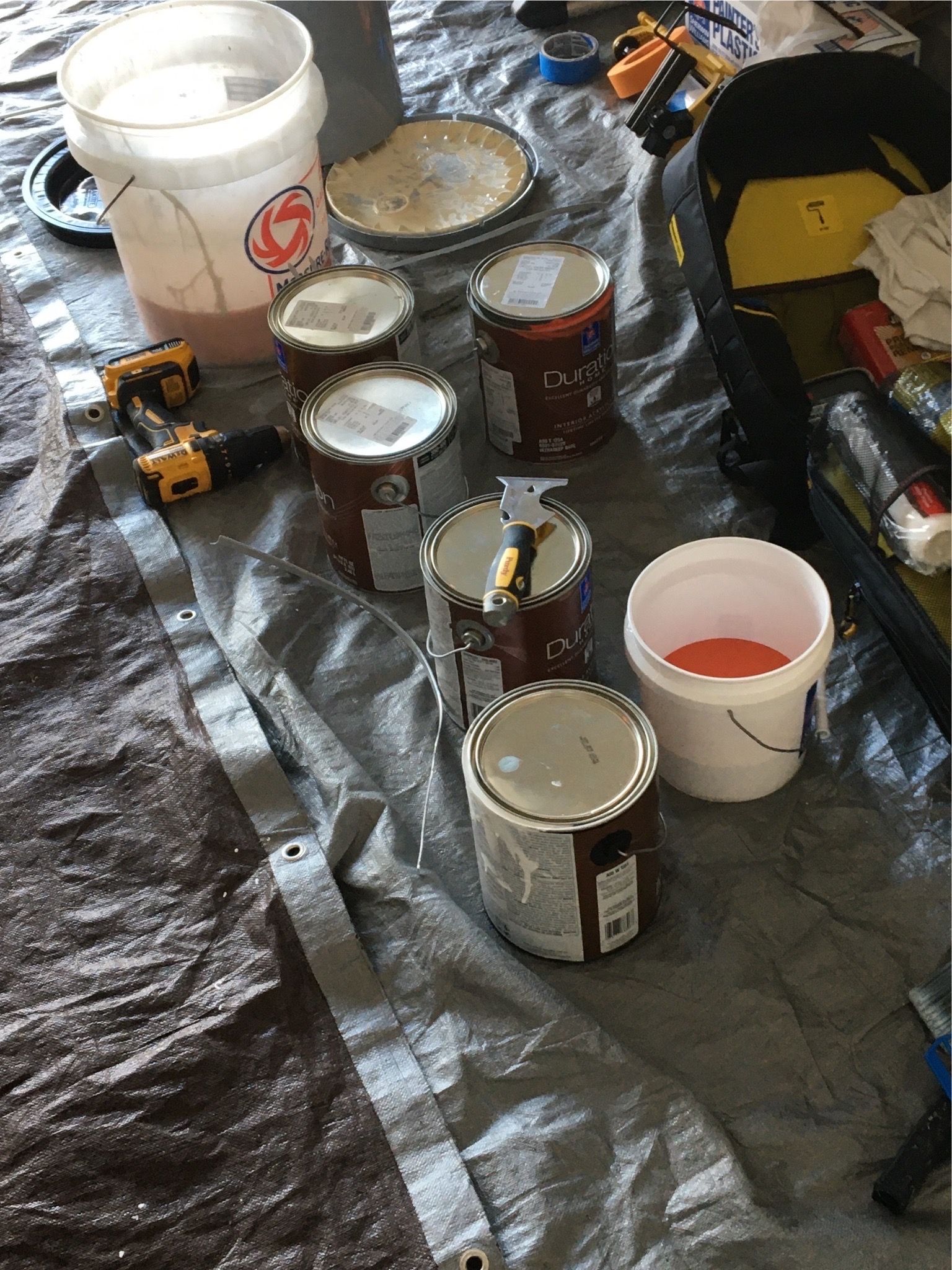 A bunch of cans of paint are sitting on a tarp on the floor.