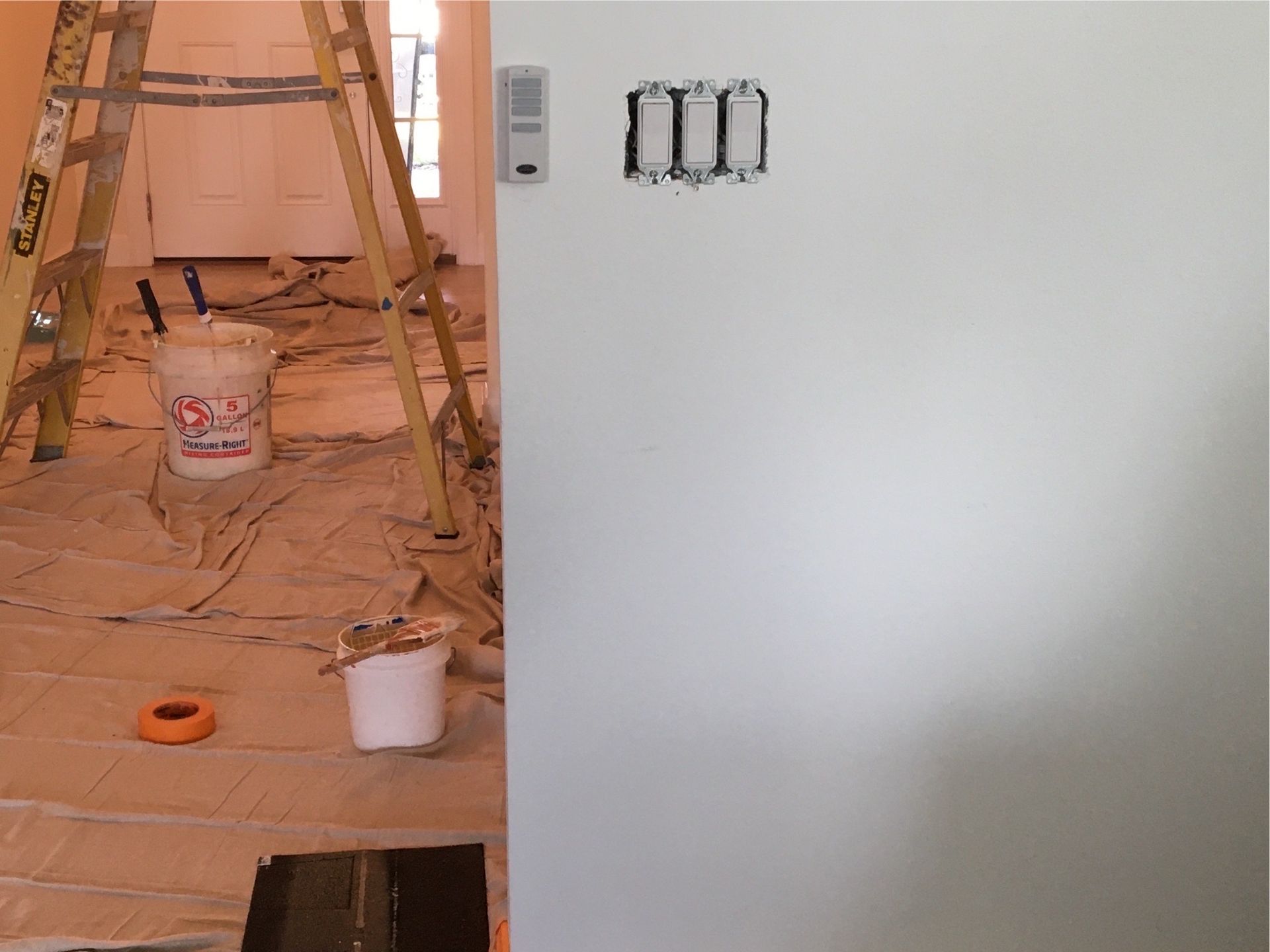 A bucket of paint sits on the floor next to a ladder