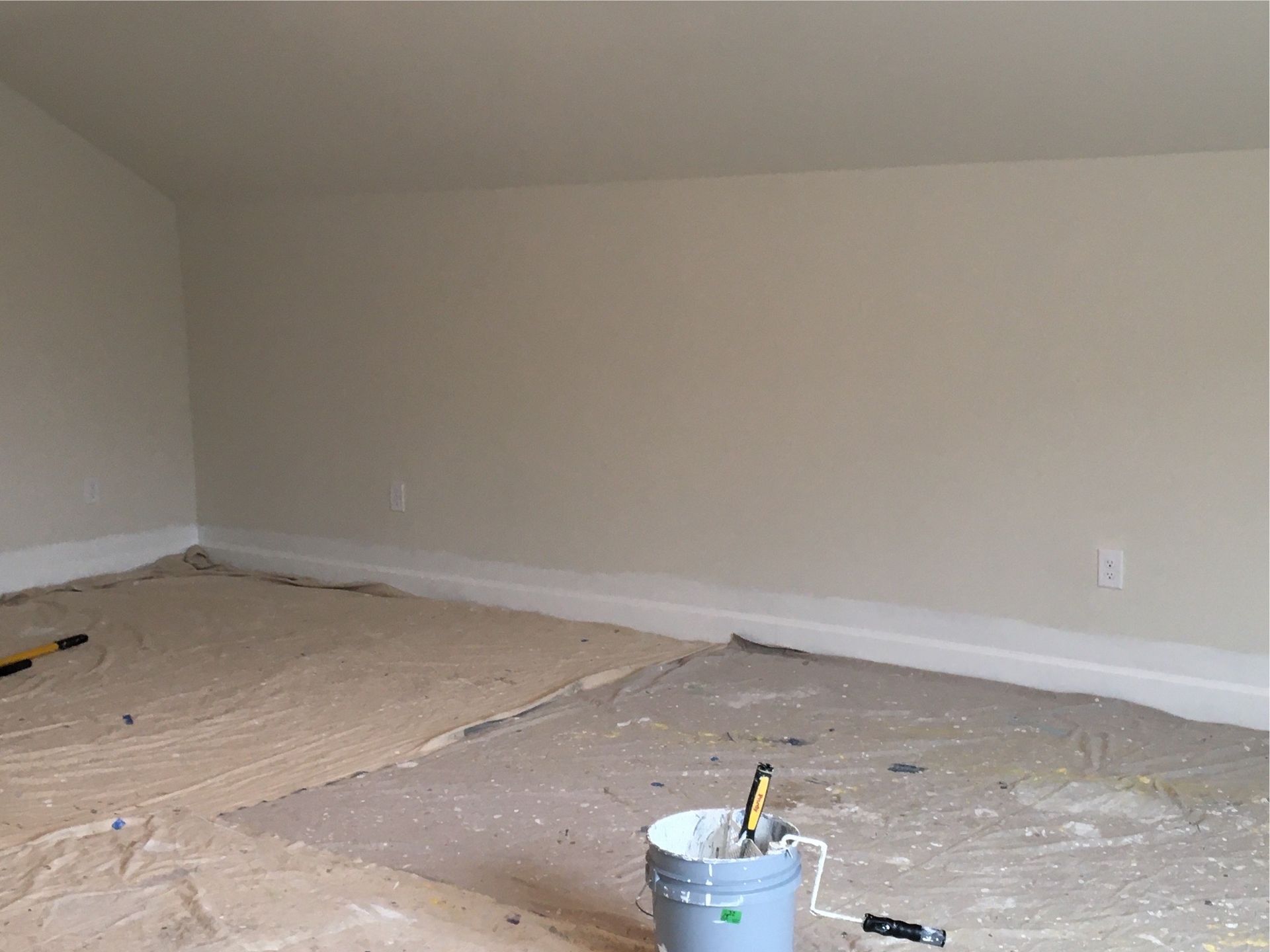 A bucket of paint is sitting on the floor in an empty room.