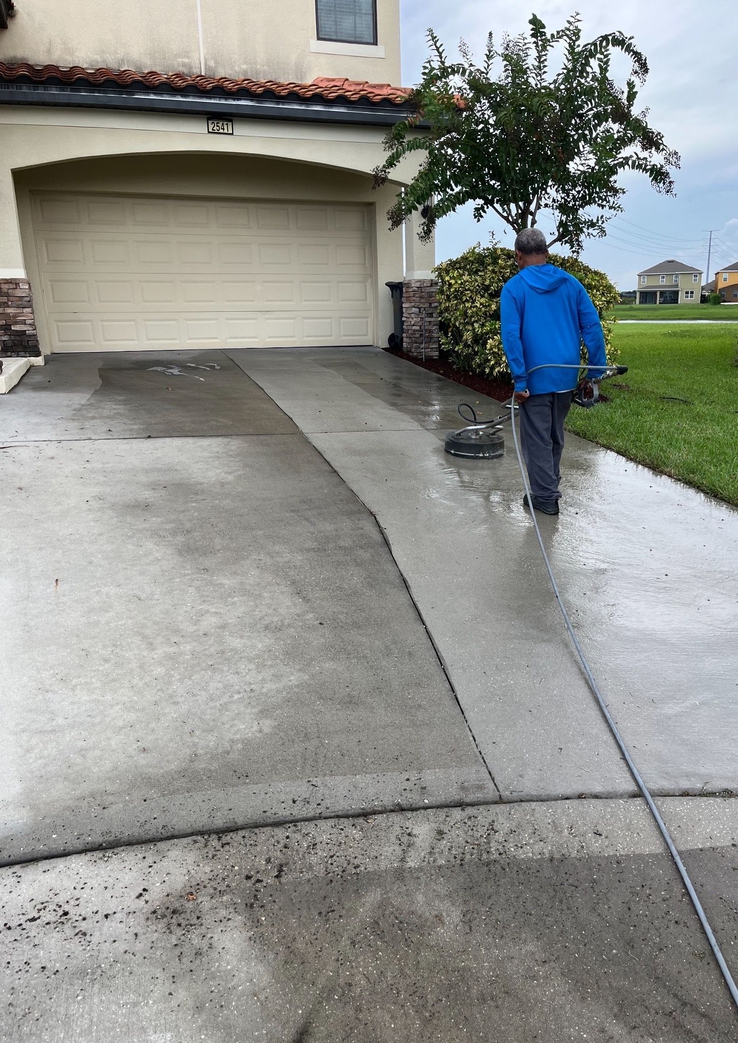 A man in a blue jacket is cleaning a driveway in front of a house.