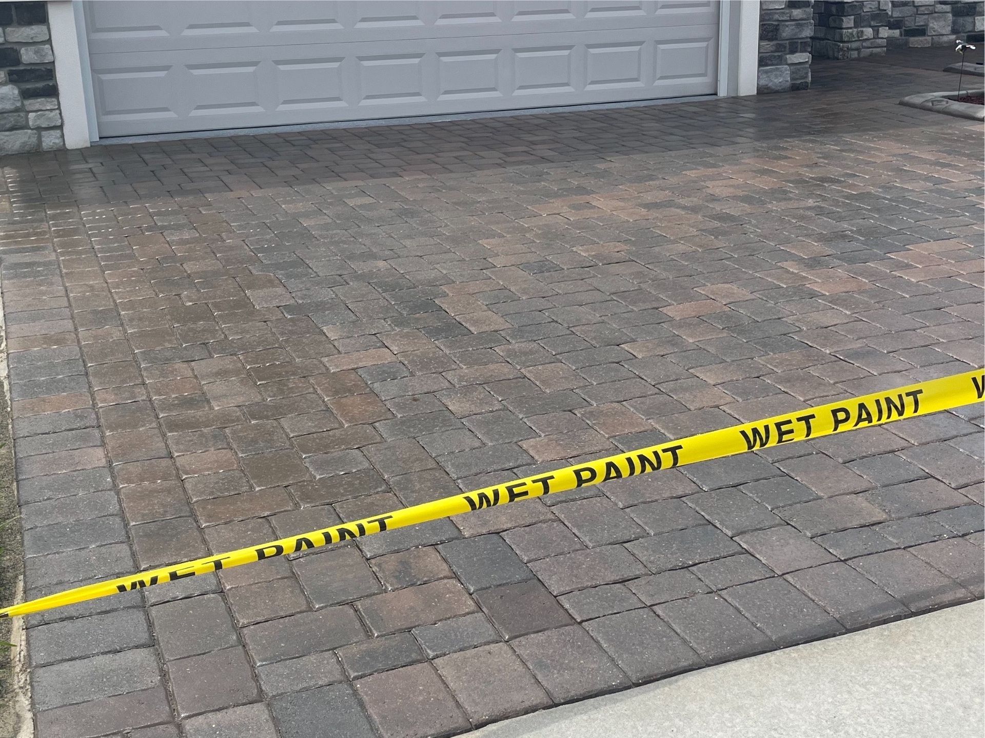 A brick driveway with a yellow tape that says wet paint