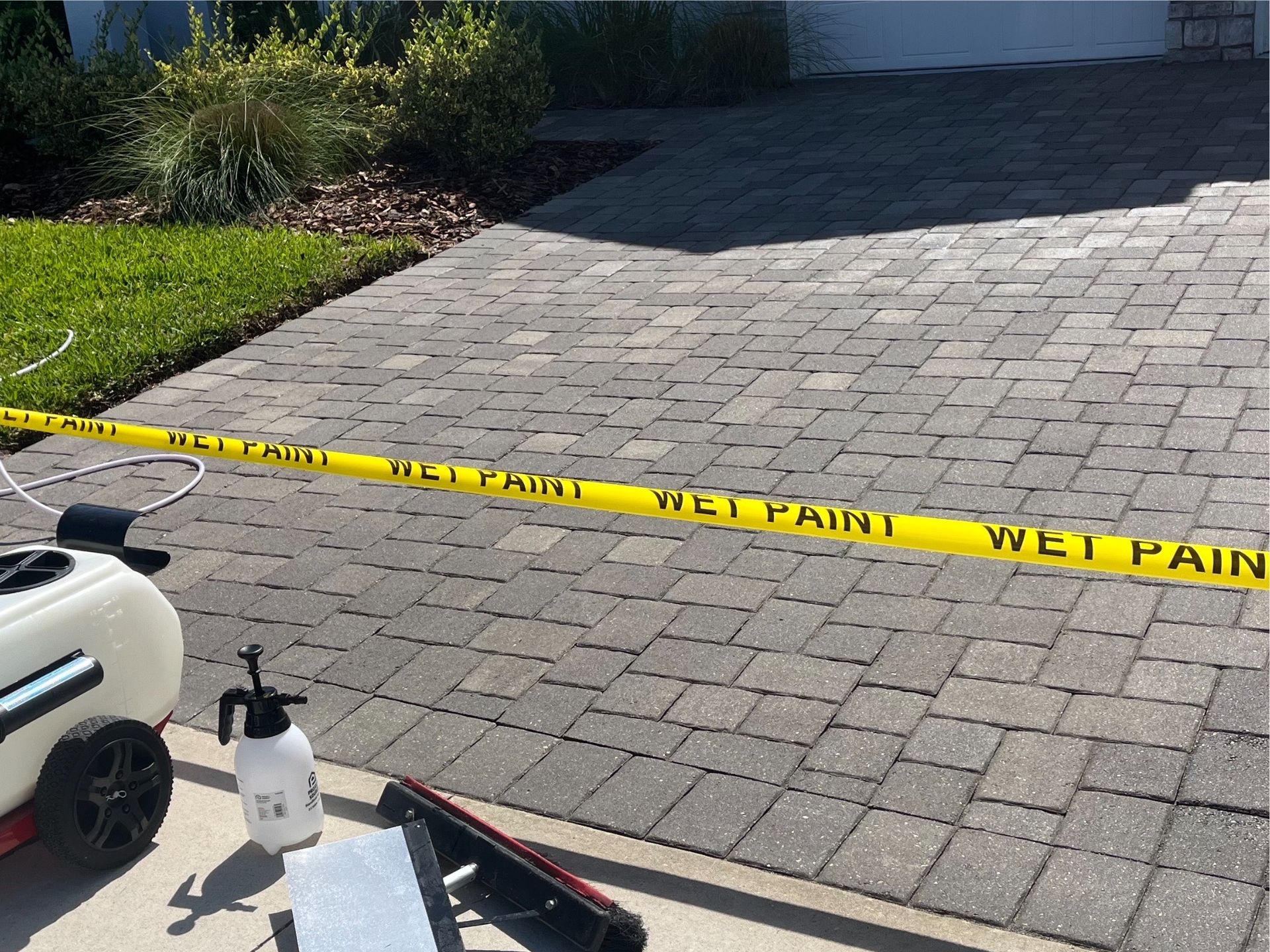 A brick driveway with a yellow tape that says wet paint on it.