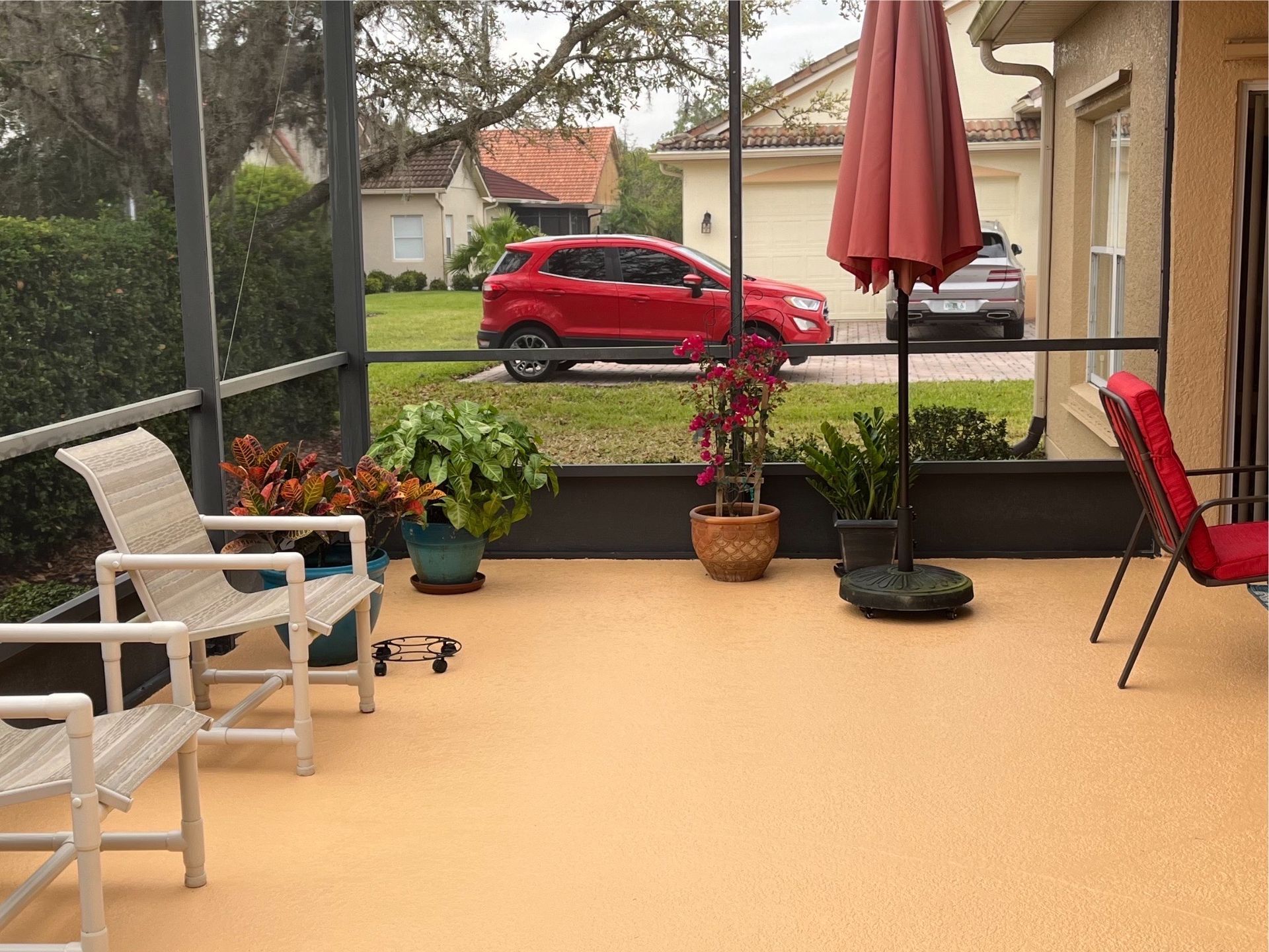 A screened in porch with chairs and umbrellas and a red car parked in the background.