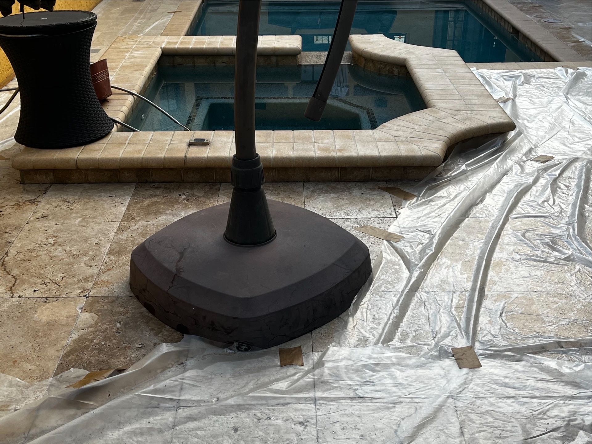 An umbrella is sitting on a patio next to a pool covered in plastic.