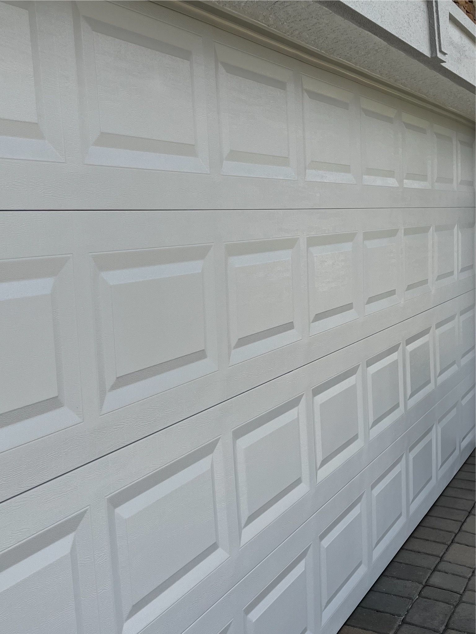 A white garage door is sitting on a brick sidewalk.
