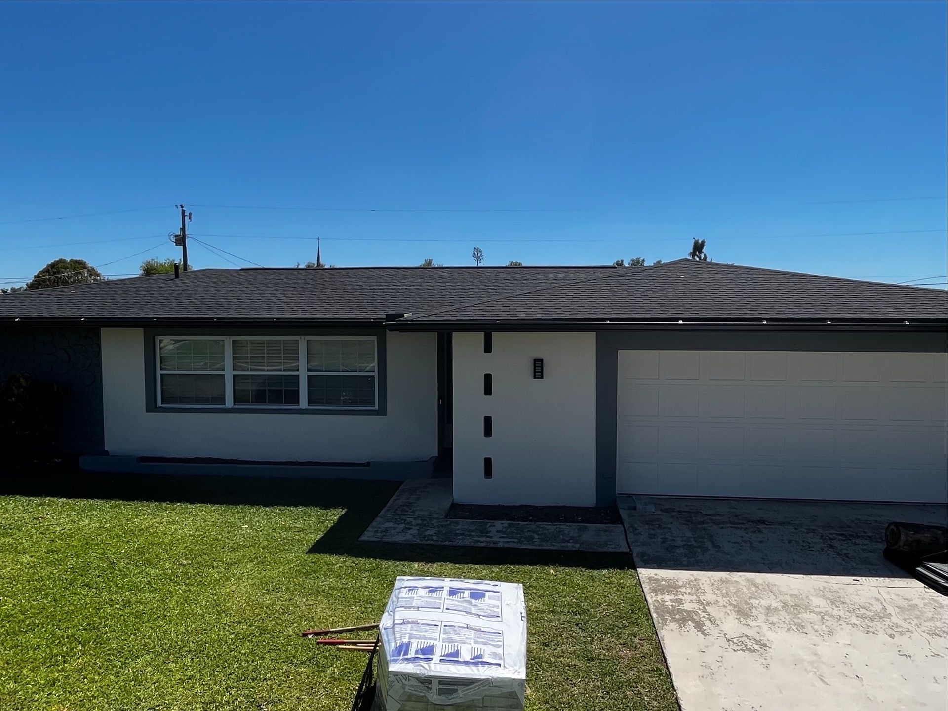 A white house with a black roof is sitting on top of a lush green lawn.