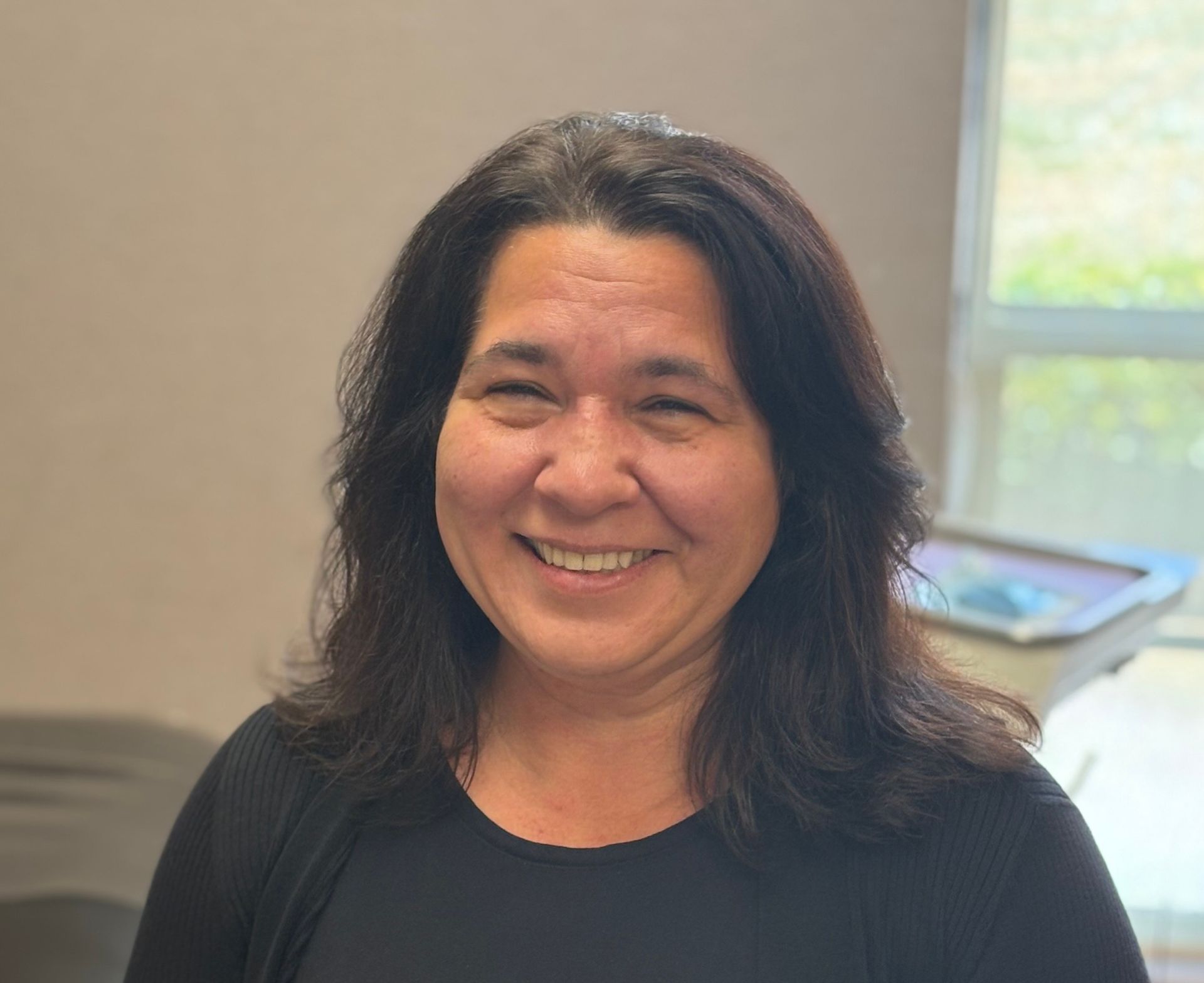 A woman wearing sunglasses and a black scrub top is smiling for the camera.