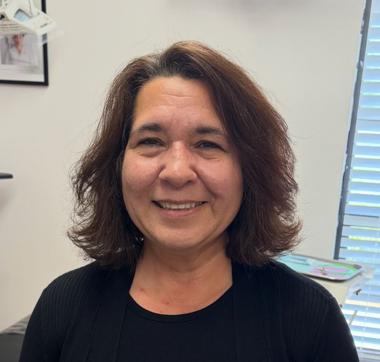 A woman wearing sunglasses and a black scrub top is smiling for the camera.