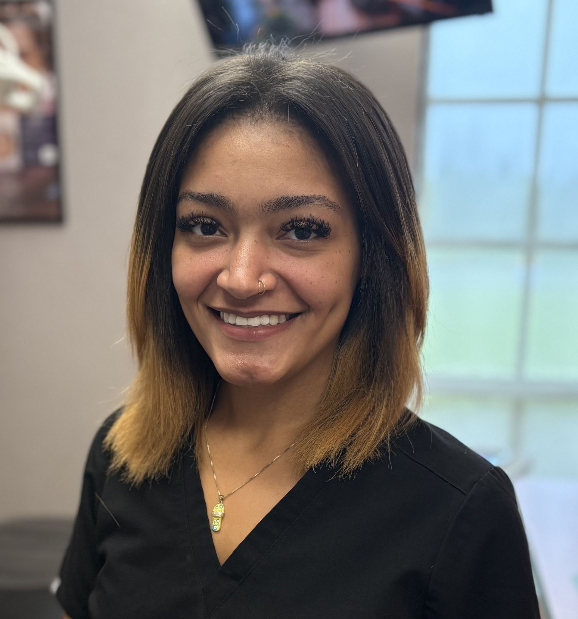A woman wearing sunglasses and a black scrub top is smiling for the camera.