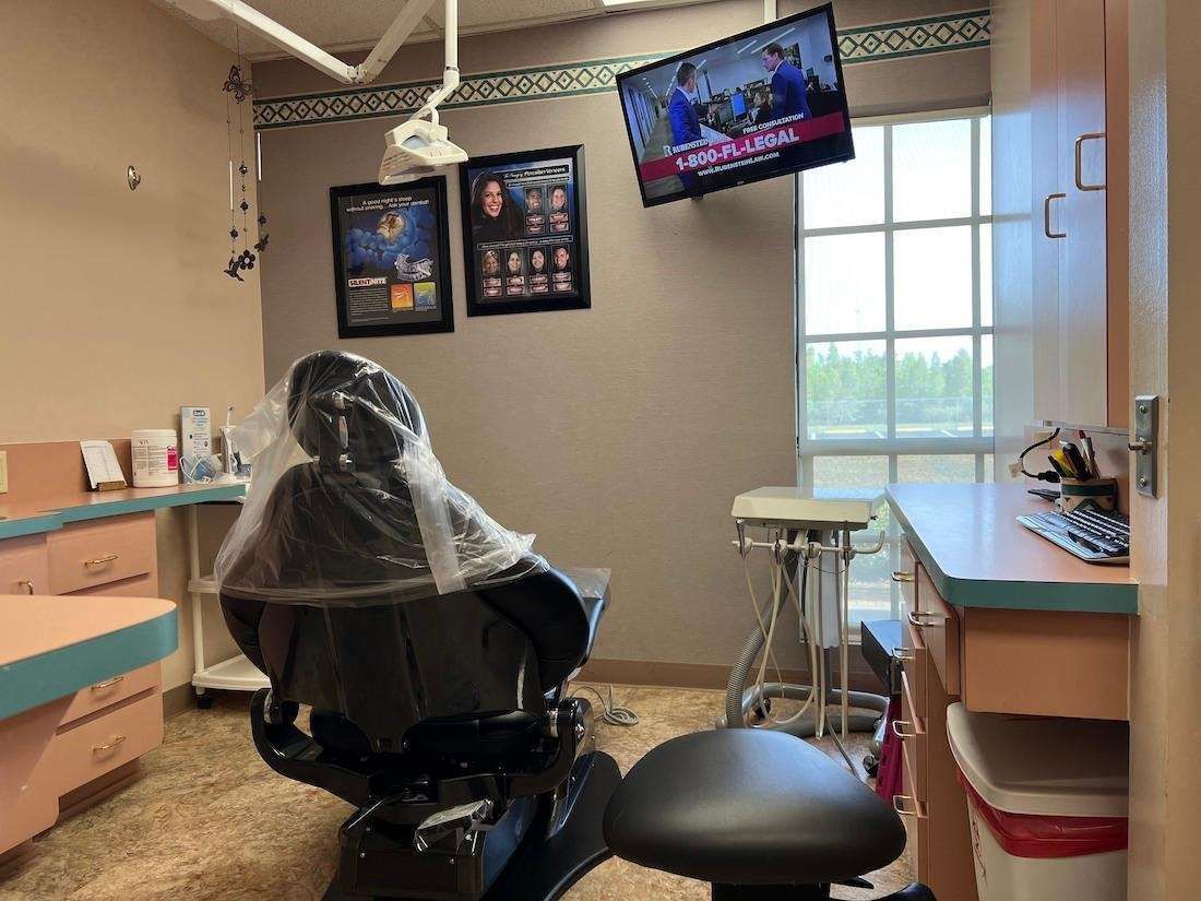 A dental office with a dental chair and a television hanging from the ceiling.