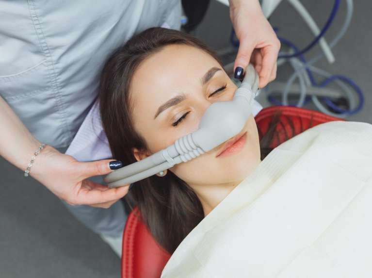 A woman is laying in a dental chair with an oxygen mask on her face.