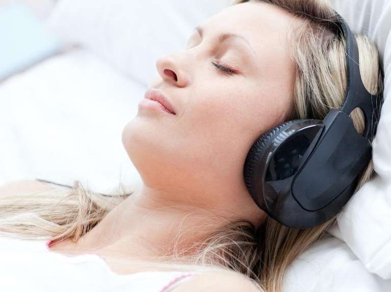 A woman wearing headphones is laying in bed with her eyes closed
