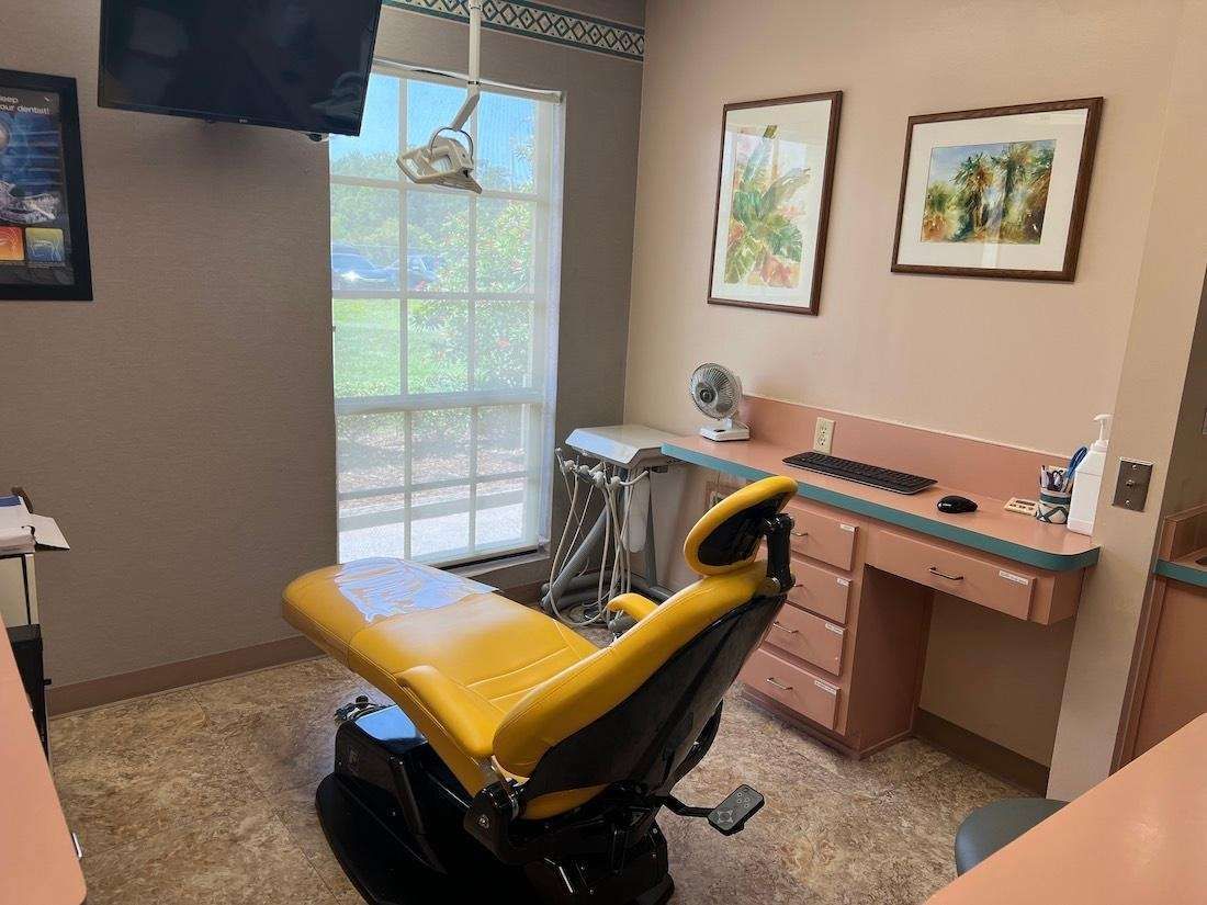 A yellow dental chair is sitting in a dental office next to a window.