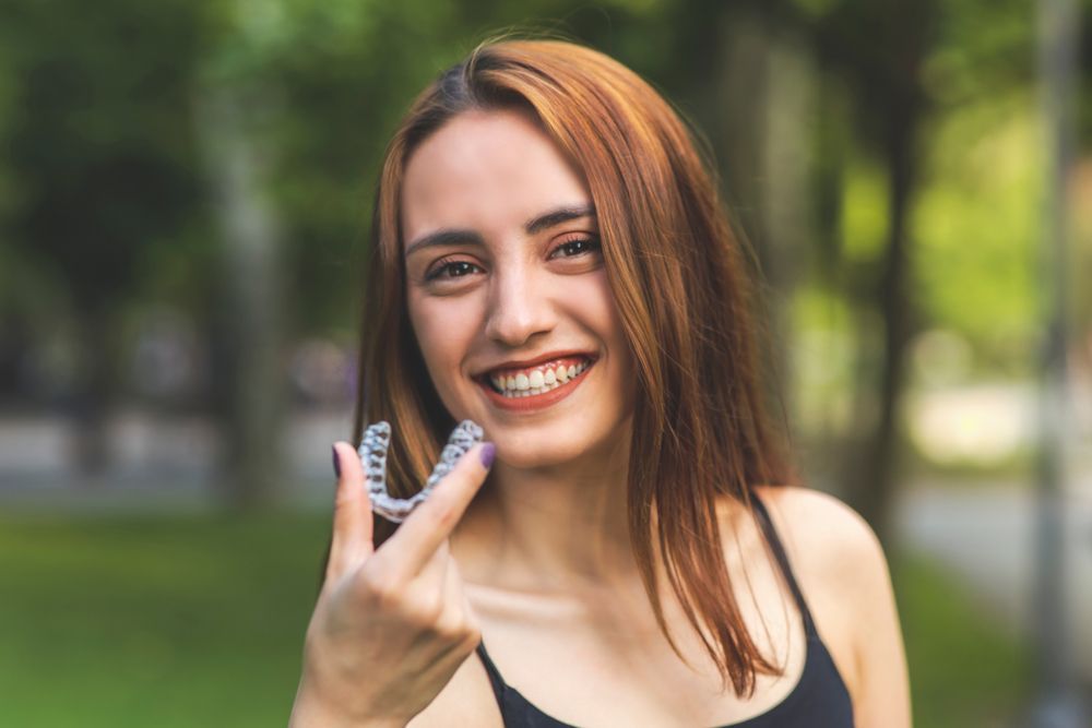 A young woman is holding a clear brace in her hand and smiling.