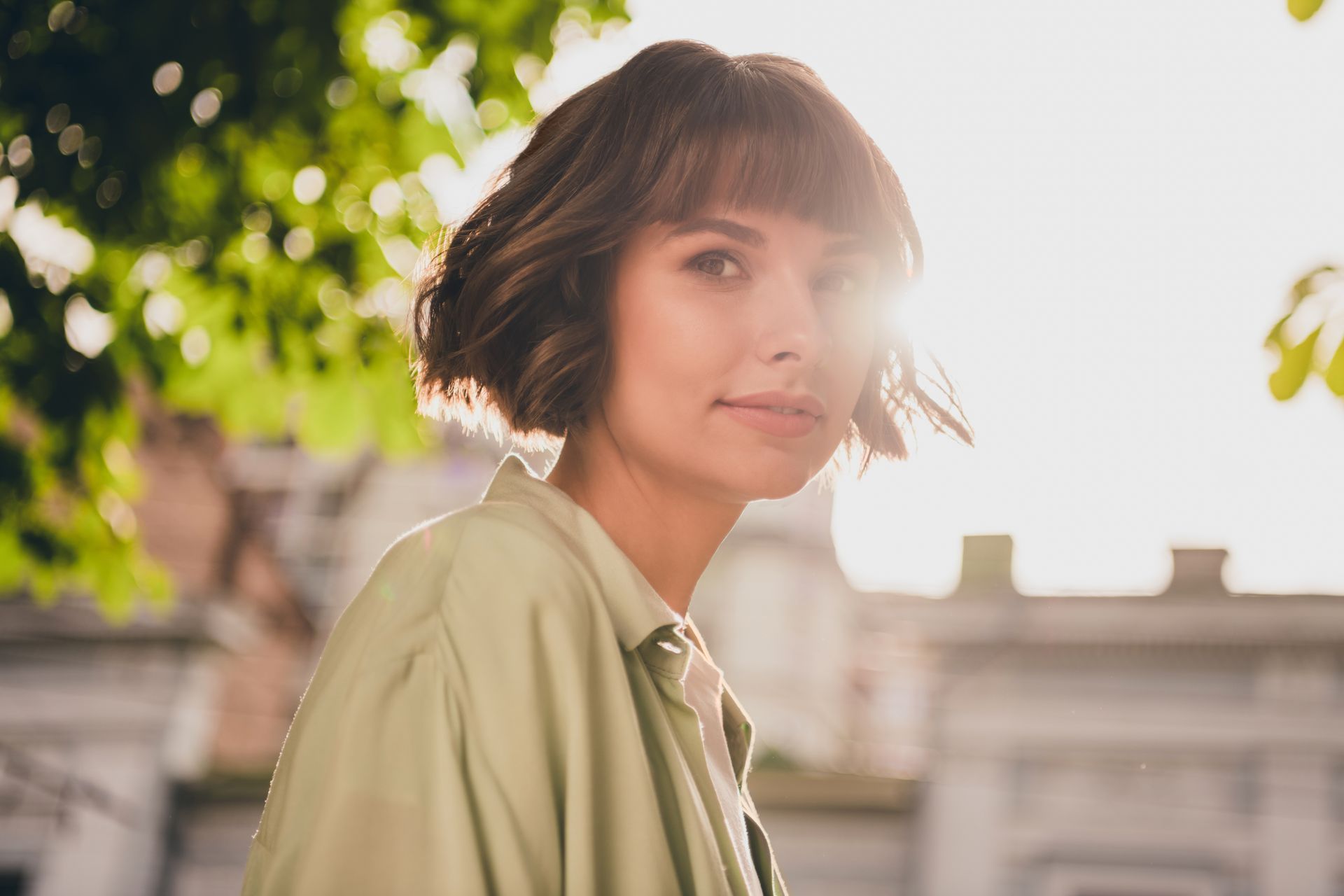 A woman with short hair is standing in front of a building and looking at the camera.