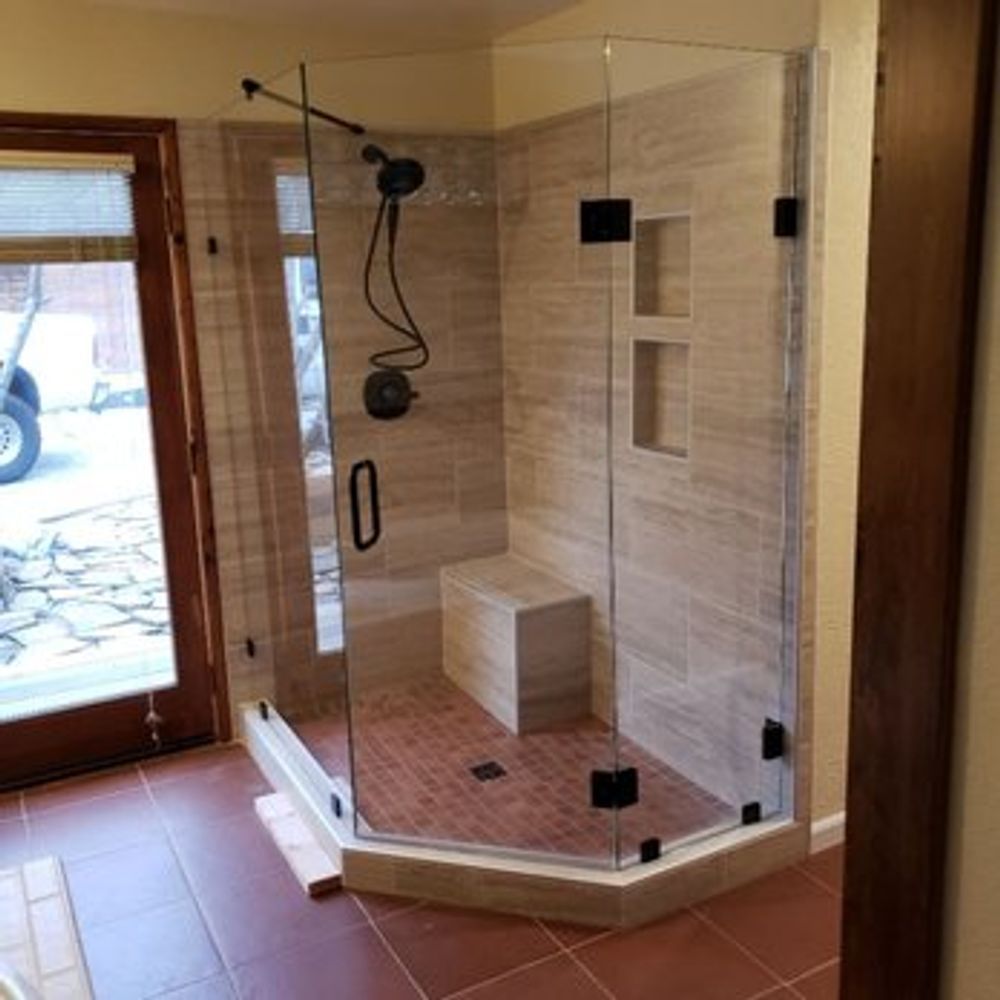 A modern, tiled shower enclosure with clear glass doors and black hardware.