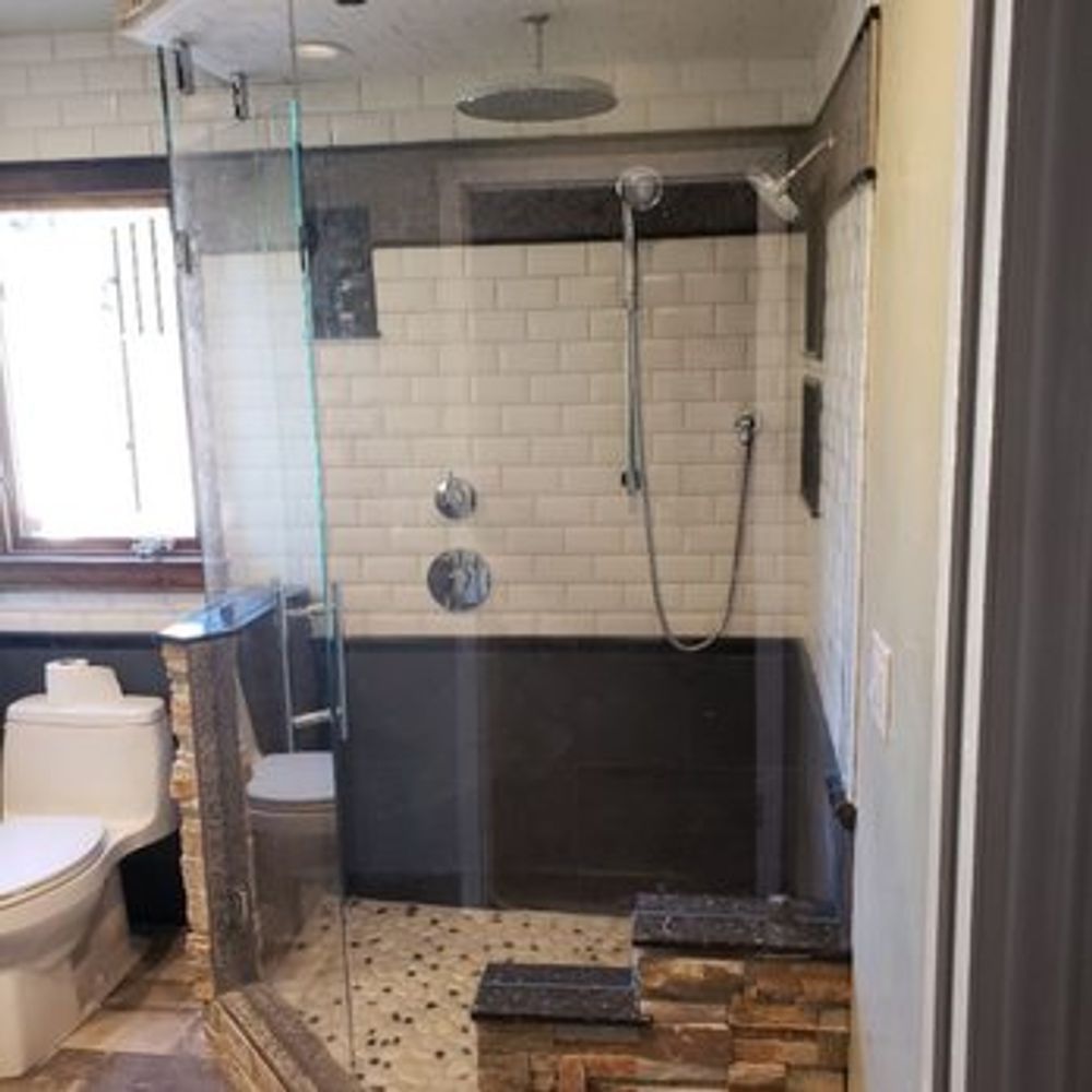Bathroom with glass shower, subway tile, dark accent wall, toilet, and a small window.