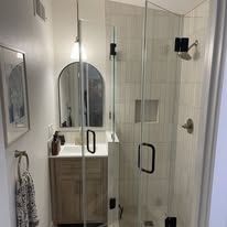 Modern bathroom with a glass shower, arched mirror, and wooden vanity.