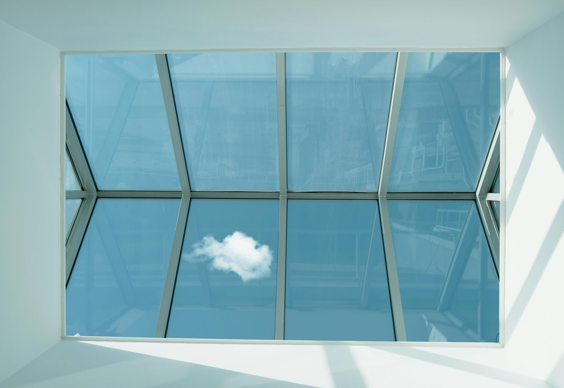 Skylight view of blue sky with a white cloud framed by white walls and structural beams.
