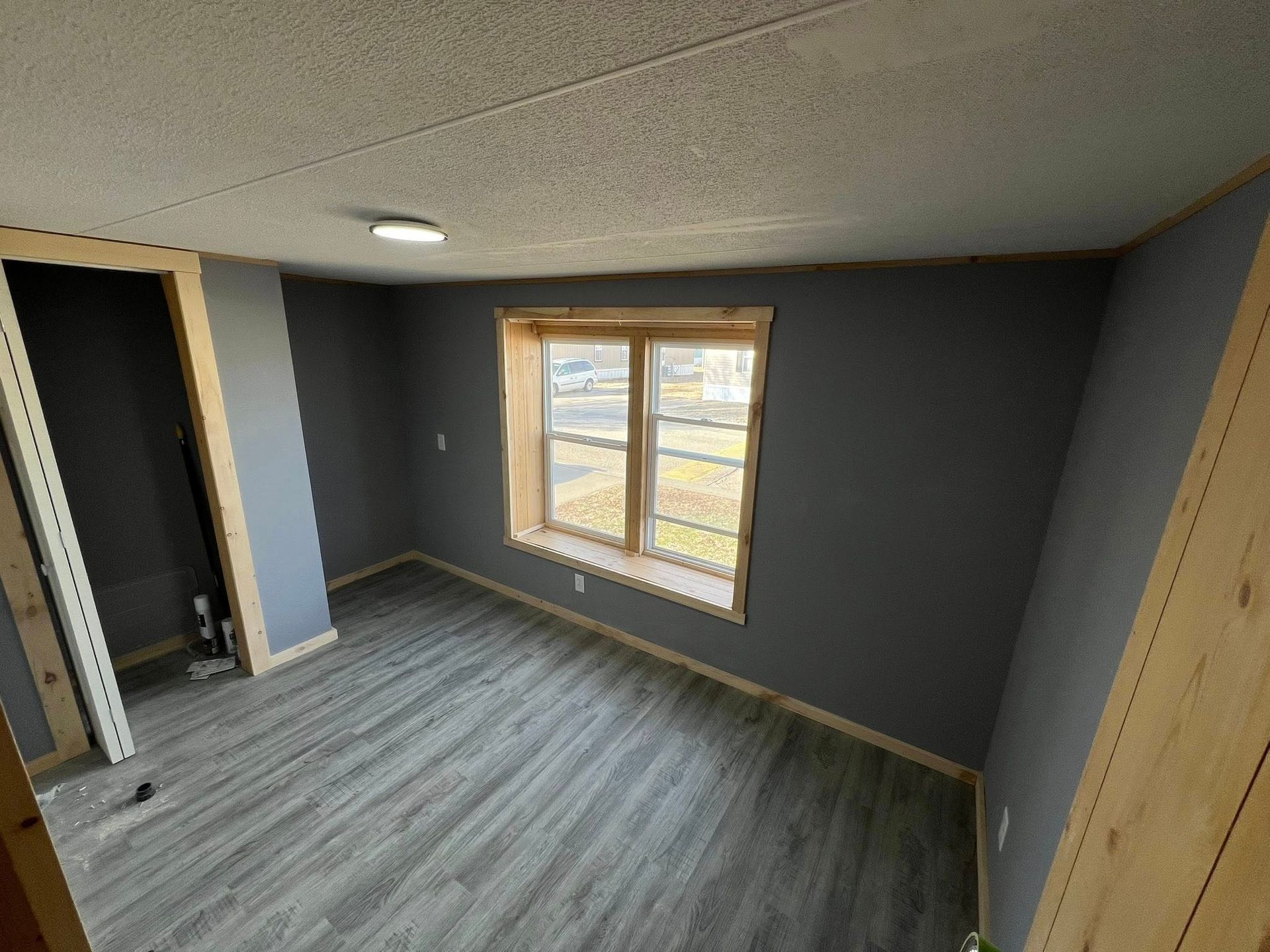 Empty room with gray walls, wood trim, and gray flooring. A window lets in light.