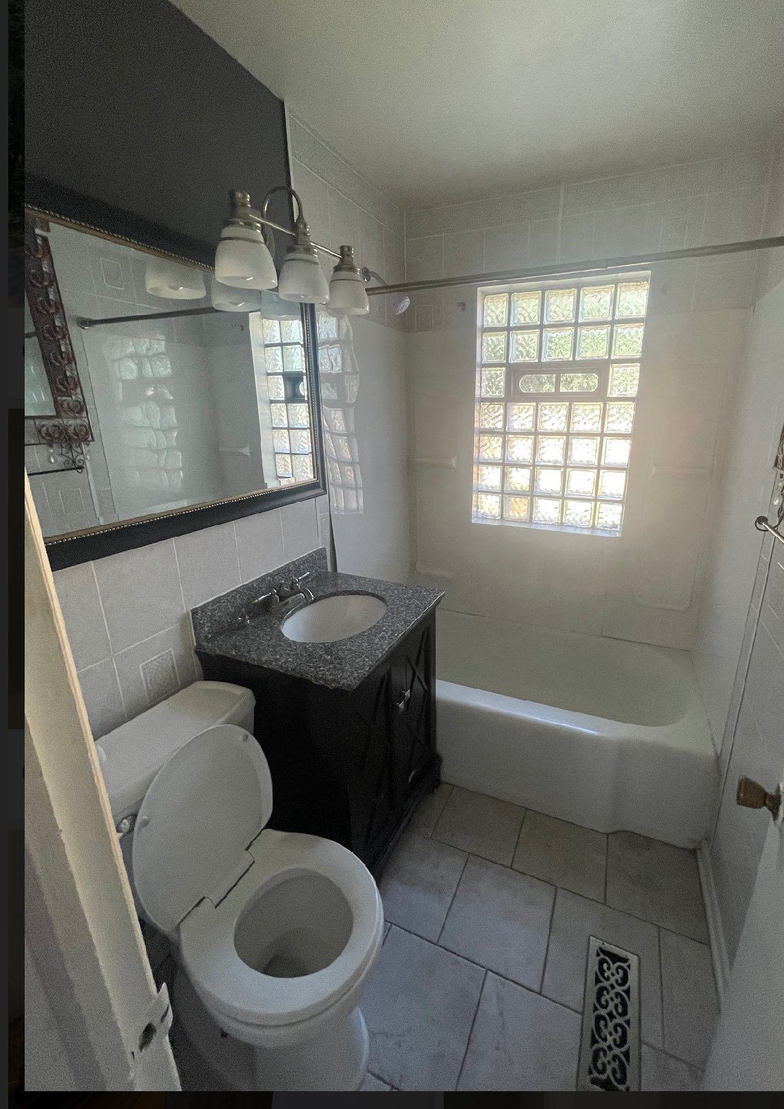 Bathroom with white tile, dark vanity, and a window with glass blocks.