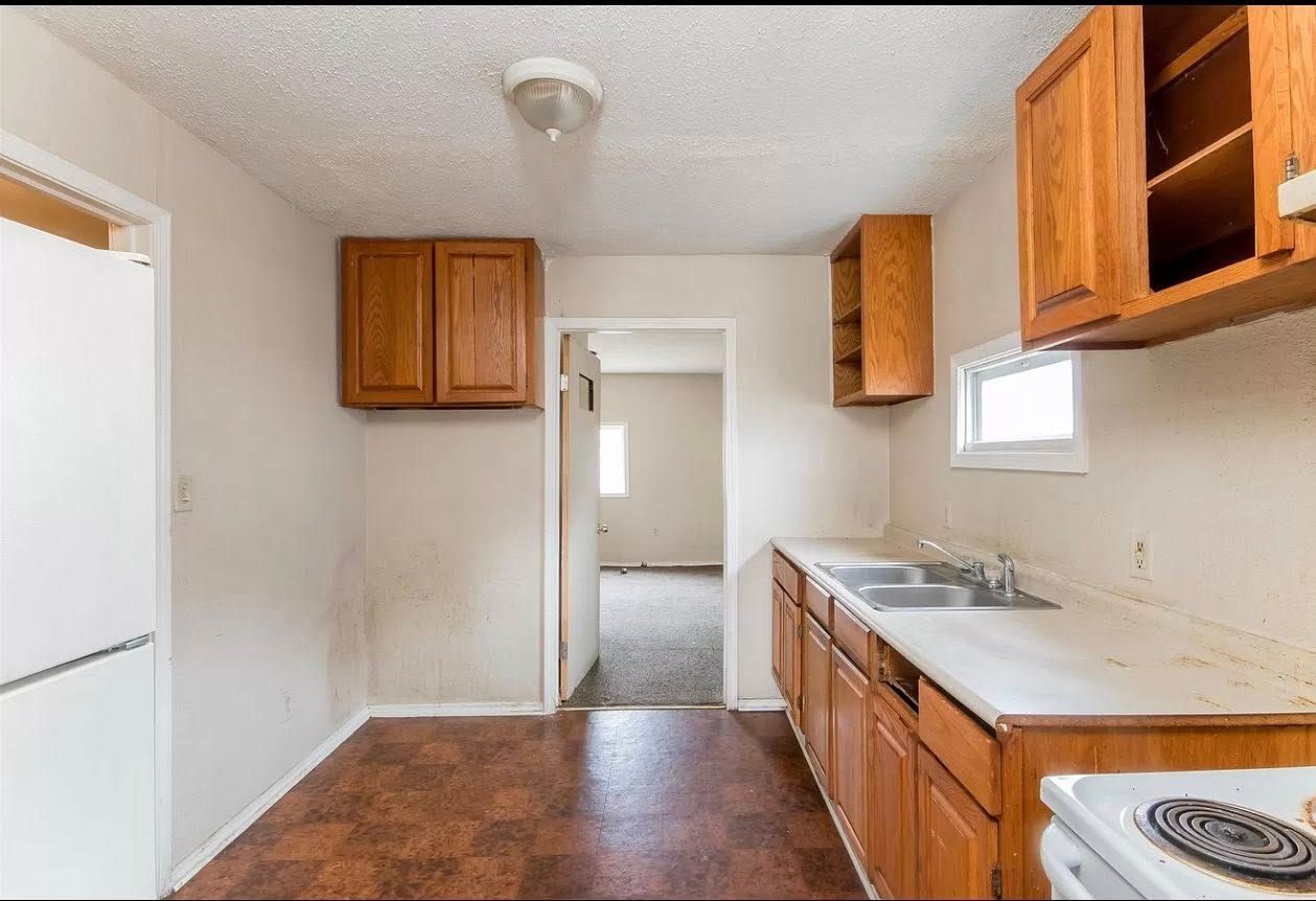 Kitchen with brown cabinets, white countertop, and doorway to another room; linoleum floor.