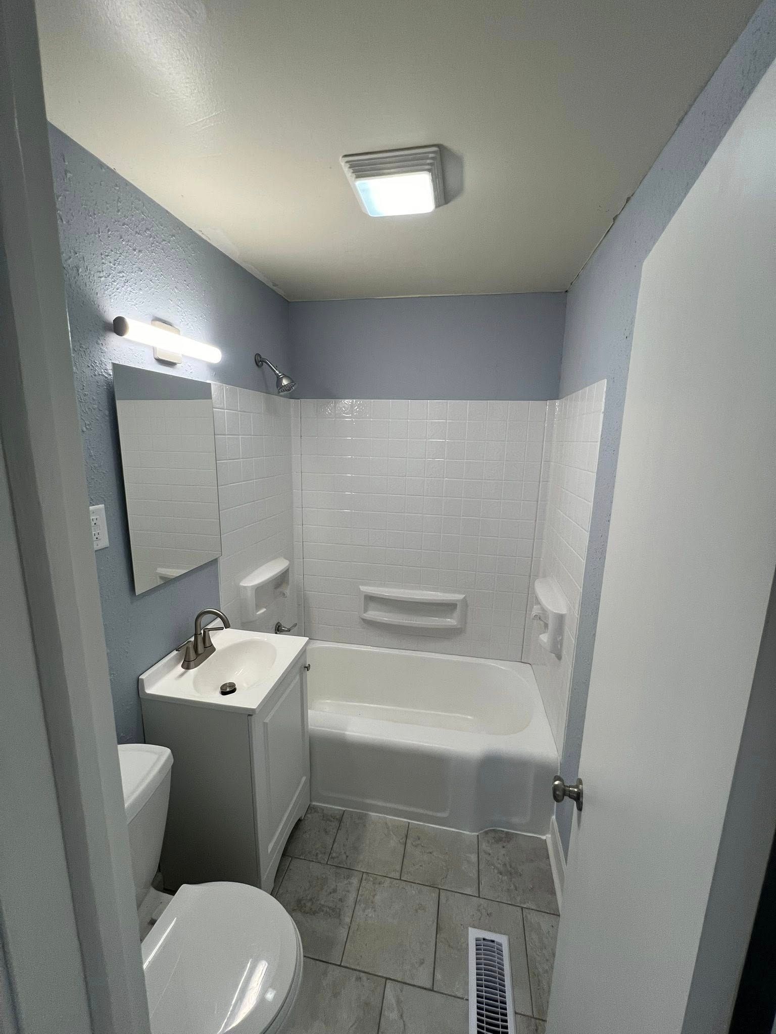 Bathroom with white tub and subway tile, a white vanity, a toilet, and blue walls.