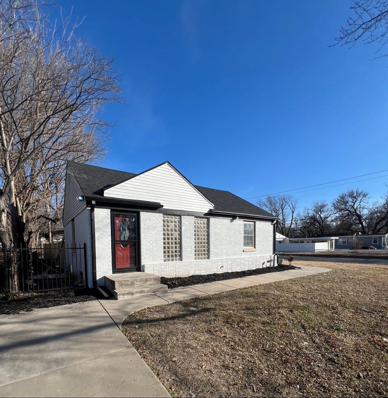 Small white house with black trim, red door, and landscaping, on a sunny day.