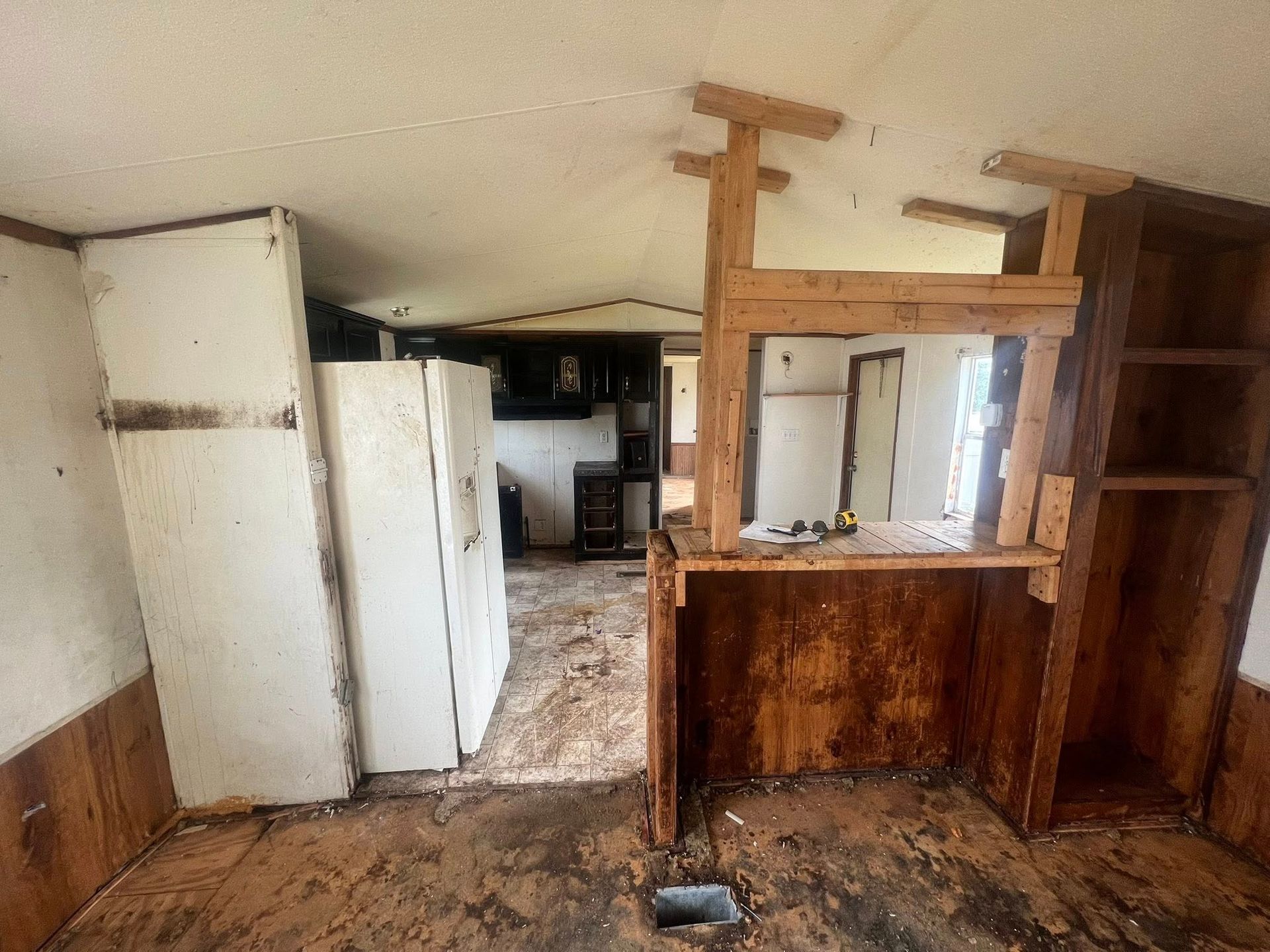 Interior of a dilapidated mobile home with peeling walls, visible appliances, and damaged shelving.
