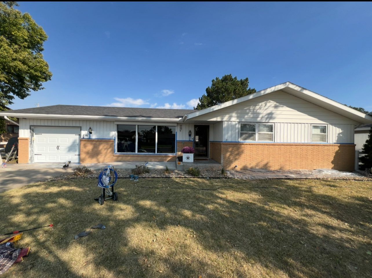 Ranch-style house with white siding, brick facade, and a two-car garage on a sunny day.